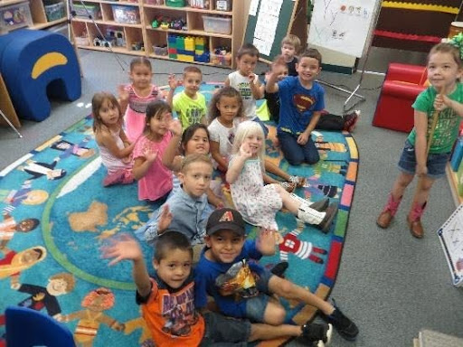 Preschool students sit on a rug smiling up at the camera.
