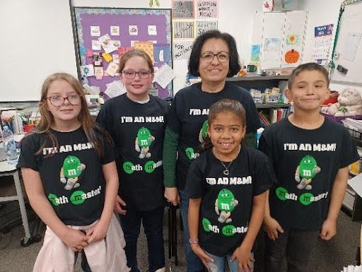 4 elementary students stand with their teacher in black t-shirts with the caption "I am an M&M!"
